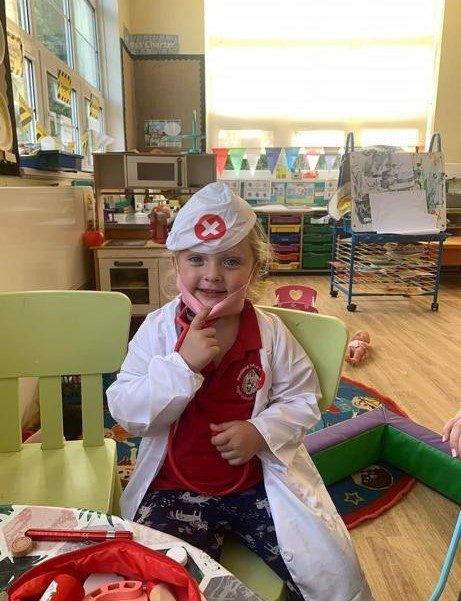 A small girl playing doctor doctor wearing a white hat and coat